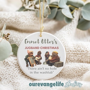 May include: White ceramic Christmas ornament featuring a scene from the Emmet Otter's Jugband Christmas special. The ornament depicts four characters playing musical instruments with the text "Emmet Otter's Jugband Christmas" and "There ain't no hole in the washtub" printed on the ornament.