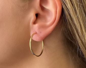 May include: A close-up of a person's ear with a gold hoop earring. The earring is simple and elegant, with a smooth, polished finish.