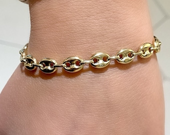 May include: A gold-toned chain bracelet with a mariner link design. The bracelet is worn on a person's wrist.