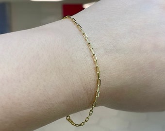 May include: A gold chain bracelet with a delicate, linked design. The bracelet is worn on a person's wrist.