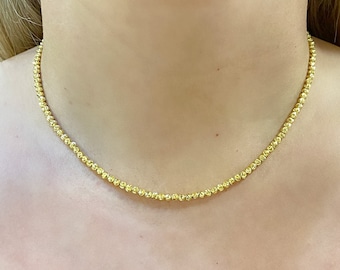 May include: A gold chain necklace with a delicate, textured design. The chain is made of small, round beads that are evenly spaced.