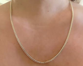 May include: A gold chain necklace with a curb link style. The chain is worn by a person, but the person is not visible in the image.