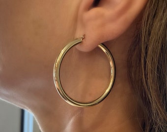 May include: Gold hoop earrings with a thick, round design. The earrings are worn in a person's ear.