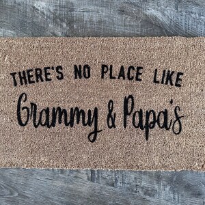 May include: A brown coir doormat with the text "There's no place like Grammy & Papa's" in black lettering.