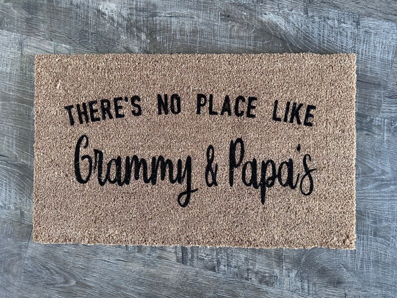 May include: A brown coir doormat with the text "There's no place like Grammy & Papa's" in black lettering.