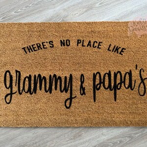 May include: A brown coir doormat with the text "There's no place like Grammy & Papa's" in black lettering.