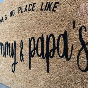 May include: A brown coir doormat with the text "There's no place like Granny & Papa's" in black lettering.