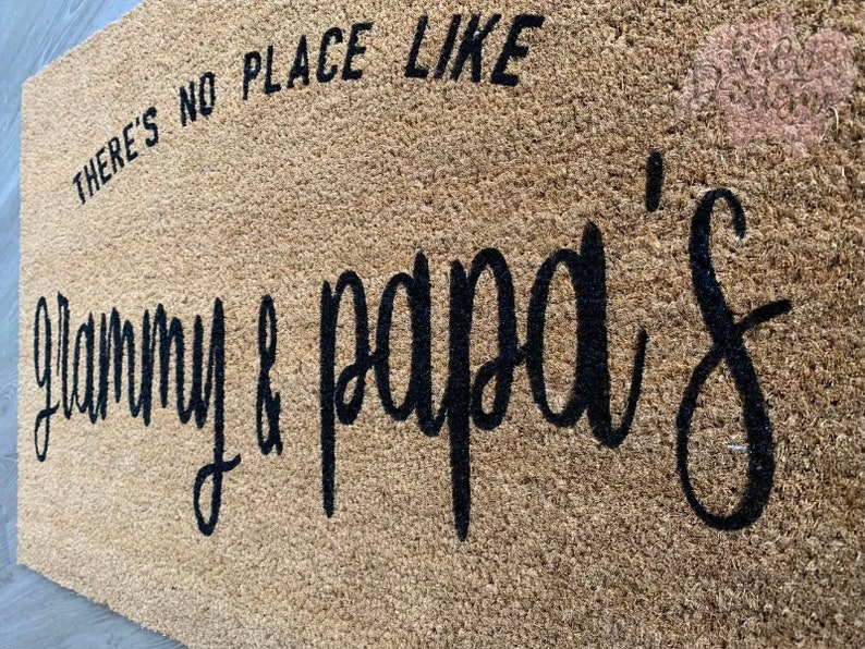 May include: A brown coir doormat with the text "There's no place like Granny & Papa's" in black lettering.