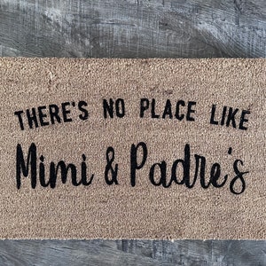 May include: A brown coir doormat with the text "There's no place like Mimi & Padres'" in black lettering.