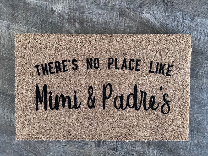 May include: A brown coir doormat with the text "There's no place like Mimi & Padres'" in black lettering.