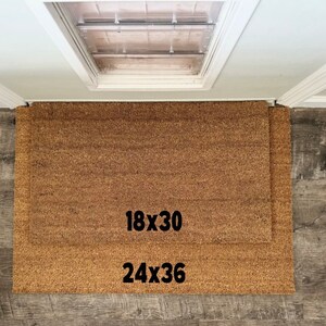 May include: Two brown coir doormats with black text. The smaller mat is labeled "18x30" and the larger mat is labeled "24x36".