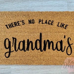 May include: A brown coir doormat with the text "There's no place like grandma's" in black lettering.