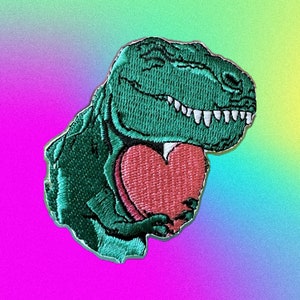 May include: Embroidered patch of a green Tyrannosaurus Rex holding a red heart. The dinosaur has white teeth and is smiling. The patch has a white border and is set against a colourful, gradient background.