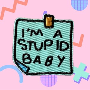 May include: A light blue fabric patch with a black border and a sticky note design. The patch has the text "I'M A STUPID BABY" in black.