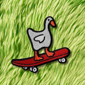 Puede incluir: Parche bordado con un ganso blanco con patas y pico naranjas, montado en una patineta roja. El parche tiene un borde negro y está sobre un fondo verde y difuso. El ganso está en una pose de patinaje.