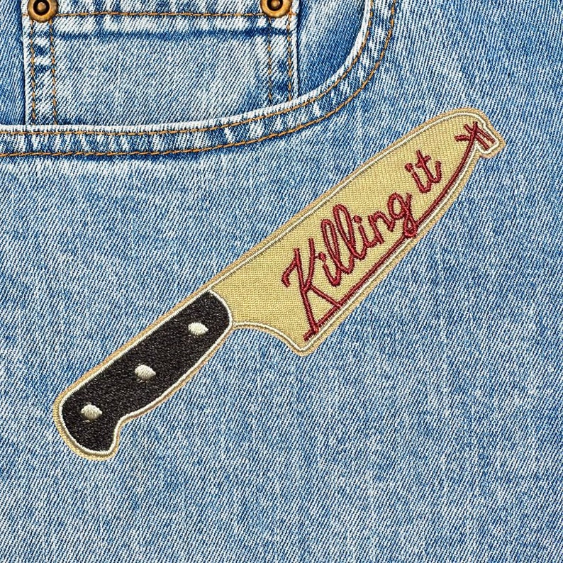 Peut inclure: Un &eacute;cusson brod&eacute; en forme de couteau de cuisine avec un manche noir et une lame beige. Le texte "Killing it" est cousu en &eacute;criture cursive rouge sur la lame. L'&eacute;cusson est fix&eacute; sur un tissu en jean bleu clair avec des coutures visibles.