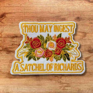May include: Embroidered patch with a floral design featuring red, pink, and yellow roses, surrounded by green leaves and wheat. The patch has the text "THOU MAY INGEST" at the top and "A SATCHEL OF RICHARDS" at the bottom, all in yellow.