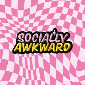 May include: Embroidered patch featuring the text "SOCIALLY AWKWARD" in pink and yellow thread, with a black outline. The patch has a black border and a small star detail. The background is a pink and white checkered pattern.
