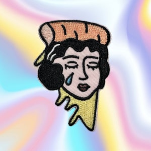 Può includere: Una toppa ricamata da stirare con una donna dei cartoni animati con una lacrima che le scende sulla guancia. Indossa un cappello marrone e ha i capelli neri. Lo sfondo è una goccia gialla.