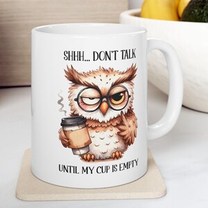 May include: White ceramic mug featuring a cartoon owl wearing glasses and holding a coffee cup. The mug has the text "SHHH... DON'T TALK" and "UNTIL MY CUP IS EMPTY". The owl is brown, beige, and white.