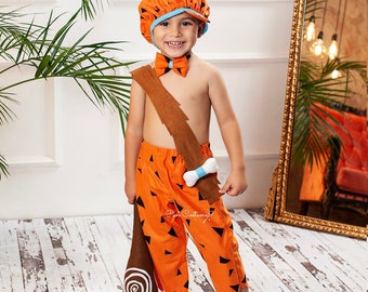 Könnte beinhalten: Ein Kind verkleidet als Zeichentrickfigur, das ein orange-braunes Kostüm mit einem braunen Gürtel, einer blauen Fliege und einem braunen Schläger trägt. Das Kostüm hat einen weißen Knochen am Gürtel und ein Muster aus orangefarbenen und schwarzen Dreiecken.