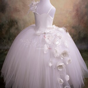 May include: White tulle dress with a satin bodice and a single strap. The dress has a large white flower embellishment on the side.