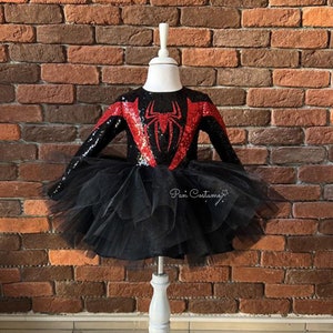 May include: Black and red sequined dress with a spider design on the front. The dress has a black tulle skirt and long sleeves.
