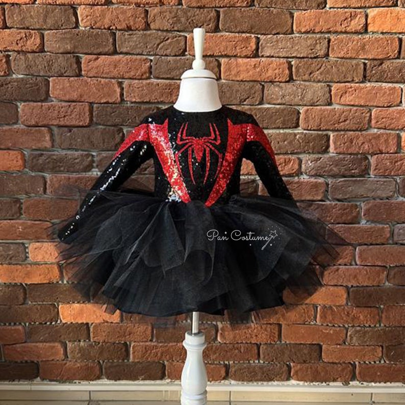 May include: Black and red sequined dress with a spider design on the front. The dress has a black tulle skirt and long sleeves.