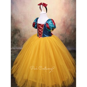 May include: A yellow tulle dress with a blue and red sequined bodice and a red bow headband. The bodice has a red and gold criss-cross design.
