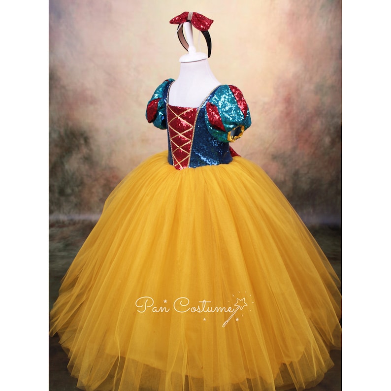 May include: A yellow tulle dress with a blue and red sequined bodice and a red bow headband. The bodice has a red and gold criss-cross design.