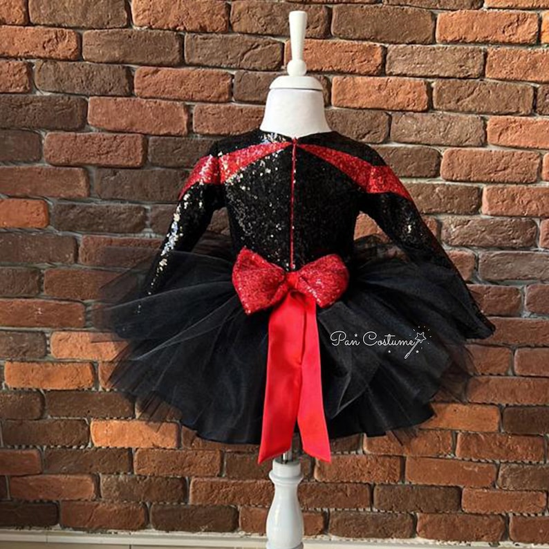 May include: Black and red sequined dress with a tulle skirt and a red bow. The dress is on a white mannequin against a brick wall.