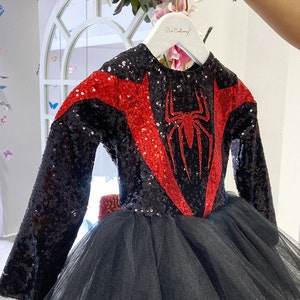 May include: Black and red sequined dress with a spider graphic on the front. The dress has a tulle skirt and long sleeves.