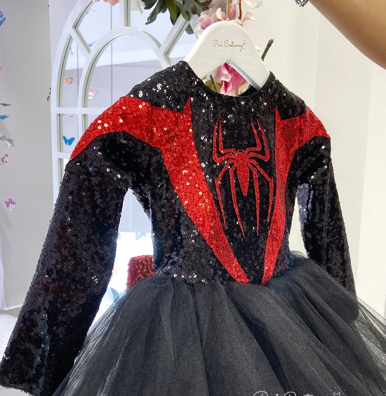 May include: Black and red sequined dress with a spider graphic on the front. The dress has a tulle skirt and long sleeves.