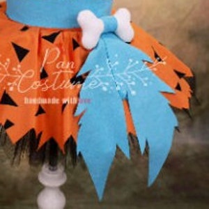 May include: Orange and black tulle tutu skirt with a blue felt dinosaur tail and a white felt bone bow. The skirt has a black elastic waistband.