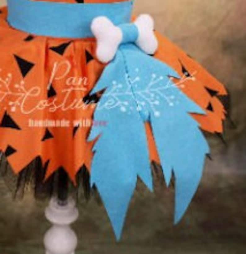 May include: Orange and black tulle tutu skirt with a blue felt dinosaur tail and a white felt bone bow. The skirt has a black elastic waistband.
