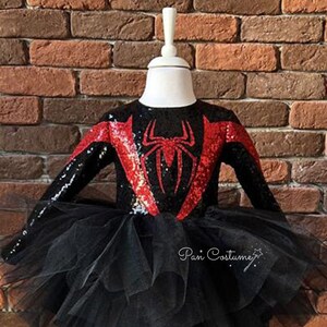 May include: Black and red sequined costume with a spider design on the bodice and a black tulle skirt. The costume is on a white mannequin. The text "Pan Costume" is visible in the bottom right corner of the image.