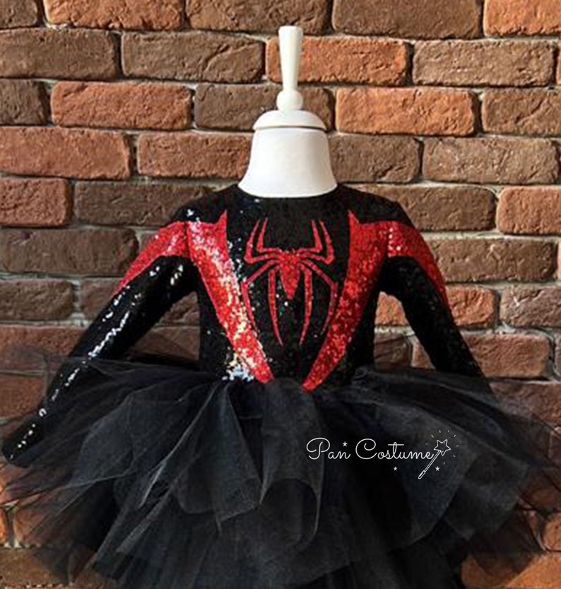 May include: Black and red sequined costume with a spider design on the bodice and a black tulle skirt. The costume is on a white mannequin. The text "Pan Costume" is visible in the bottom right corner of the image.