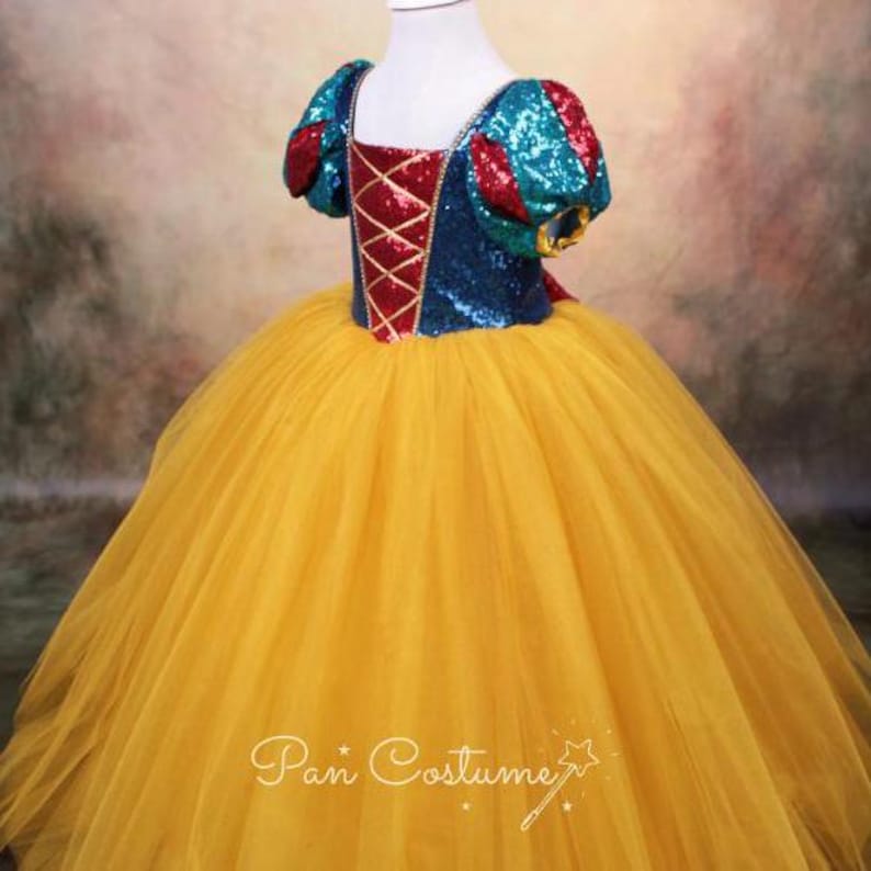 May include: A yellow tulle dress with a blue, red, and green sequined bodice. The bodice has a red and gold criss-cross design. The dress is for a child.