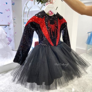 May include: Black and red sequined dress with a spider design on the bodice and a black tulle skirt. The dress is on a white hanger.