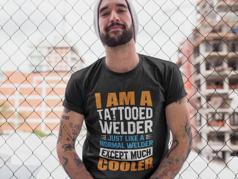 May include: A man wearing a black t-shirt with the text "I am a tattooed welder - Just like a normal welder except much cooler".