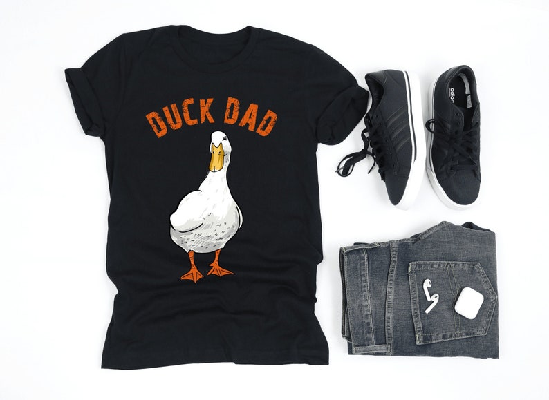Może przedstawiać: Czarny T-shirt z napisem "Duck Dad" w pomarańczowych literach i ilustracją białego kaczora.