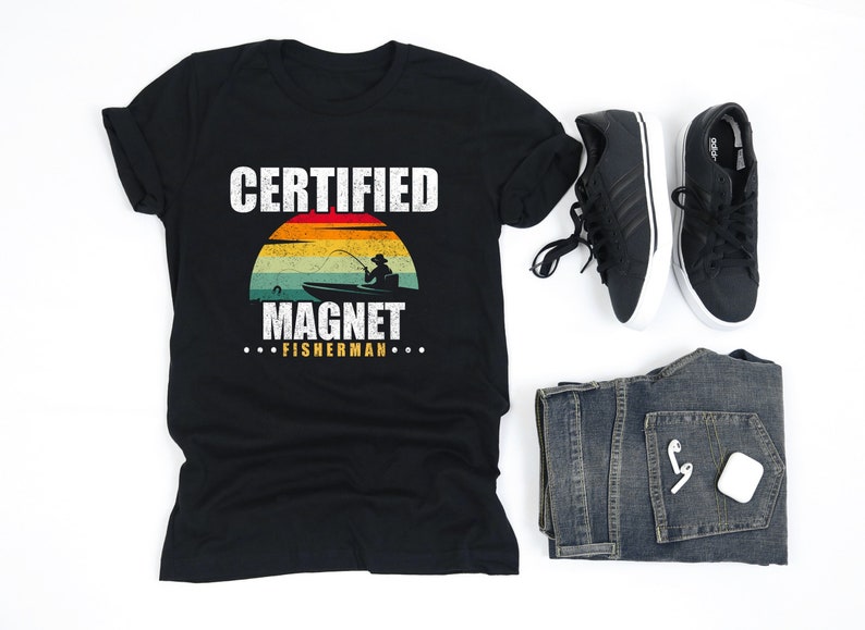 May include: Black t-shirt with a vintage-style graphic that says "Certified Magnet Fisherman". The graphic features a sunset with a person fishing from a boat.