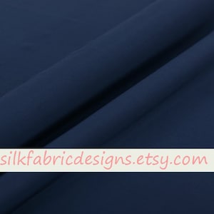 Pode incluir: Um close-up de um tecido azul escuro com um brilho sutil. O tecido é liso e tem um leve drapeado. O texto "silkfabricdesigns.etsy.com" é impresso em uma faixa branca na parte inferior da imagem.