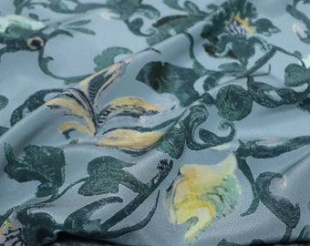 May include: Blue silk fabric with a green and yellow floral pattern. The fabric is draped and has a soft, flowing texture.