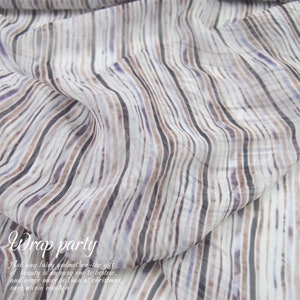 Pode incluir: Um tecido transparente drapeado com um padrão listrado em tons de branco, cinza, marrom e roxo. O tecido é dobrado, criando dobras macias. O texto na parte inferior diz "Wrap party" e uma citação sobre beleza.