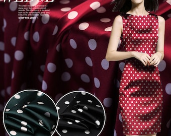 May include: Two fabric swatches with white polka dots on a dark background. One swatch is black and the other is dark green. The fabric is smooth and shiny. The background is a red fabric with white polka dots.