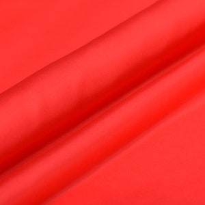 Puede incluir: Primer plano de una tela de color rojo brillante con una textura suave y sedosa. La tela está doblada en diagonal, creando un aspecto suave y fluido.