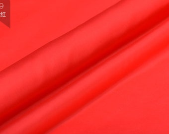 May include: A close-up of a bright red fabric with a smooth, silky texture. The fabric is folded in a diagonal pattern, creating a soft, flowing look.