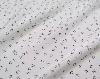 May include: White silk fabric with a repeating pattern of black horseshoes. The fabric is smooth and has a subtle sheen.