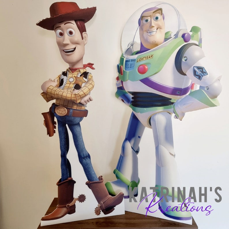 May include: Two cardboard stand-up figures of popular cartoon characters, Woody and Buzz Lightyear from the Toy Story franchise. Woody is wearing his signature cowboy hat, vest, and jeans. Buzz Lightyear is wearing his iconic space ranger suit.